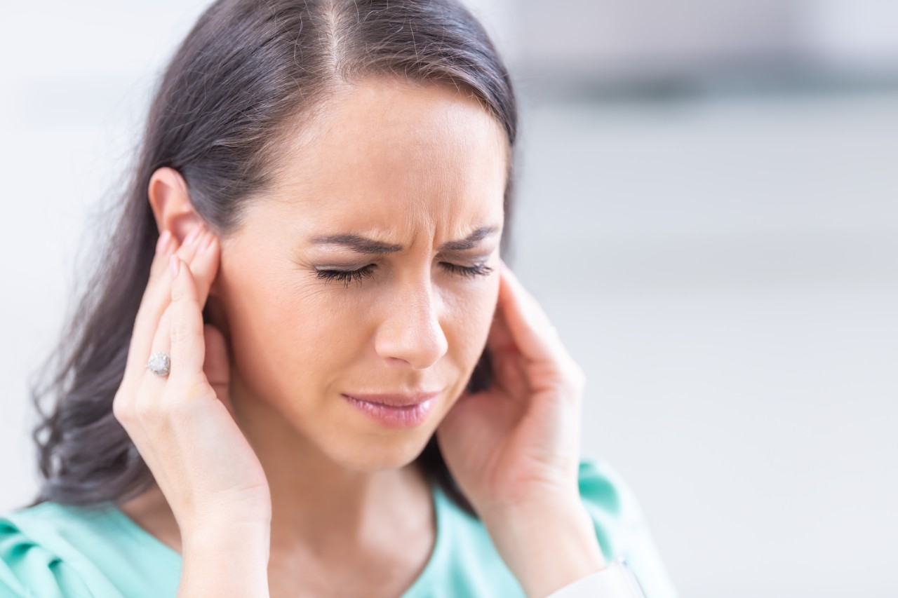 Jeune femme exprimant la douleur en tenant ses deux oreilles